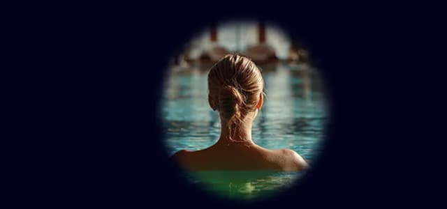 A person seen from behind, relaxing in a swimming pool inside a calm, softly lit space.