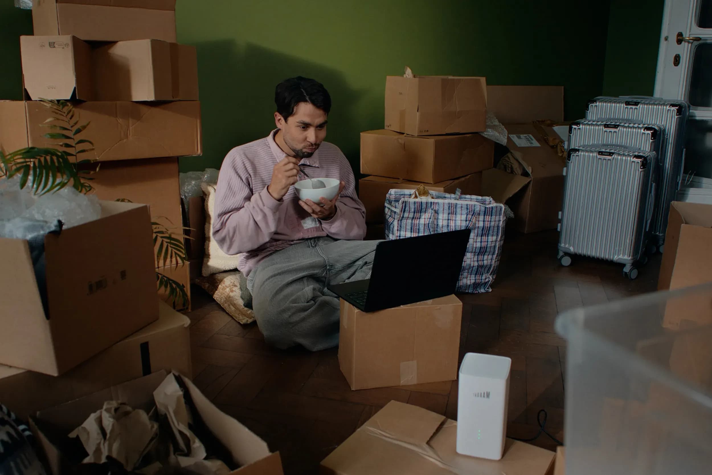A guy sitting on the ground watching his laptop with moving boxes surrounding him.