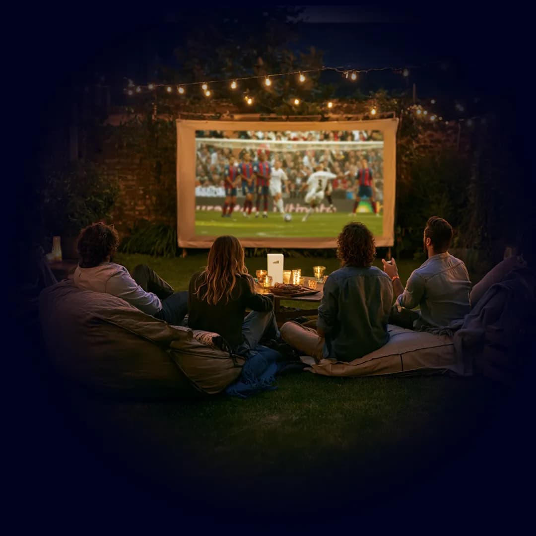 Friends watching football on an outdoor screen at night, TADAAM modem on the table.