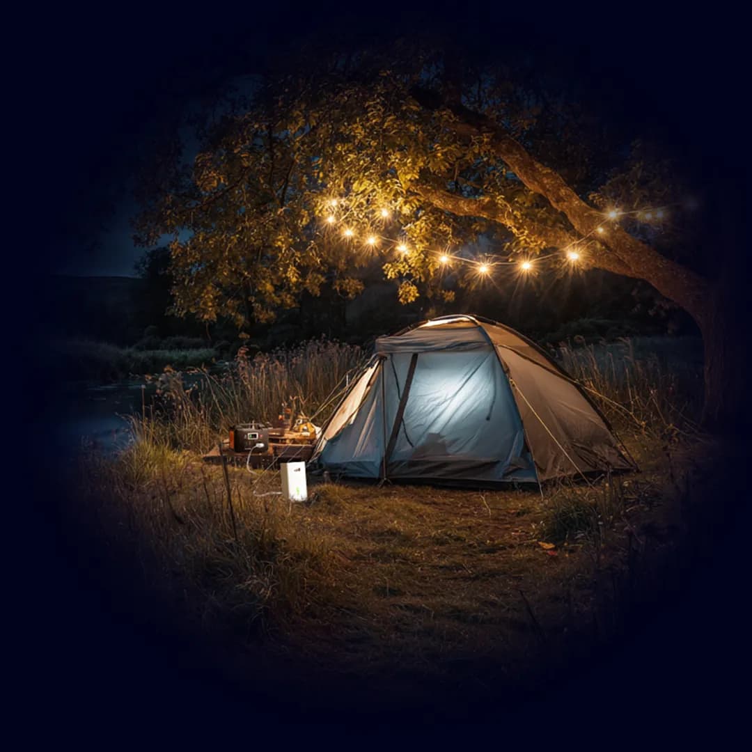 Tent glowing at night by a river, with string lights in a tree and a TADAAM modem set up outside — internet wherever you camp.