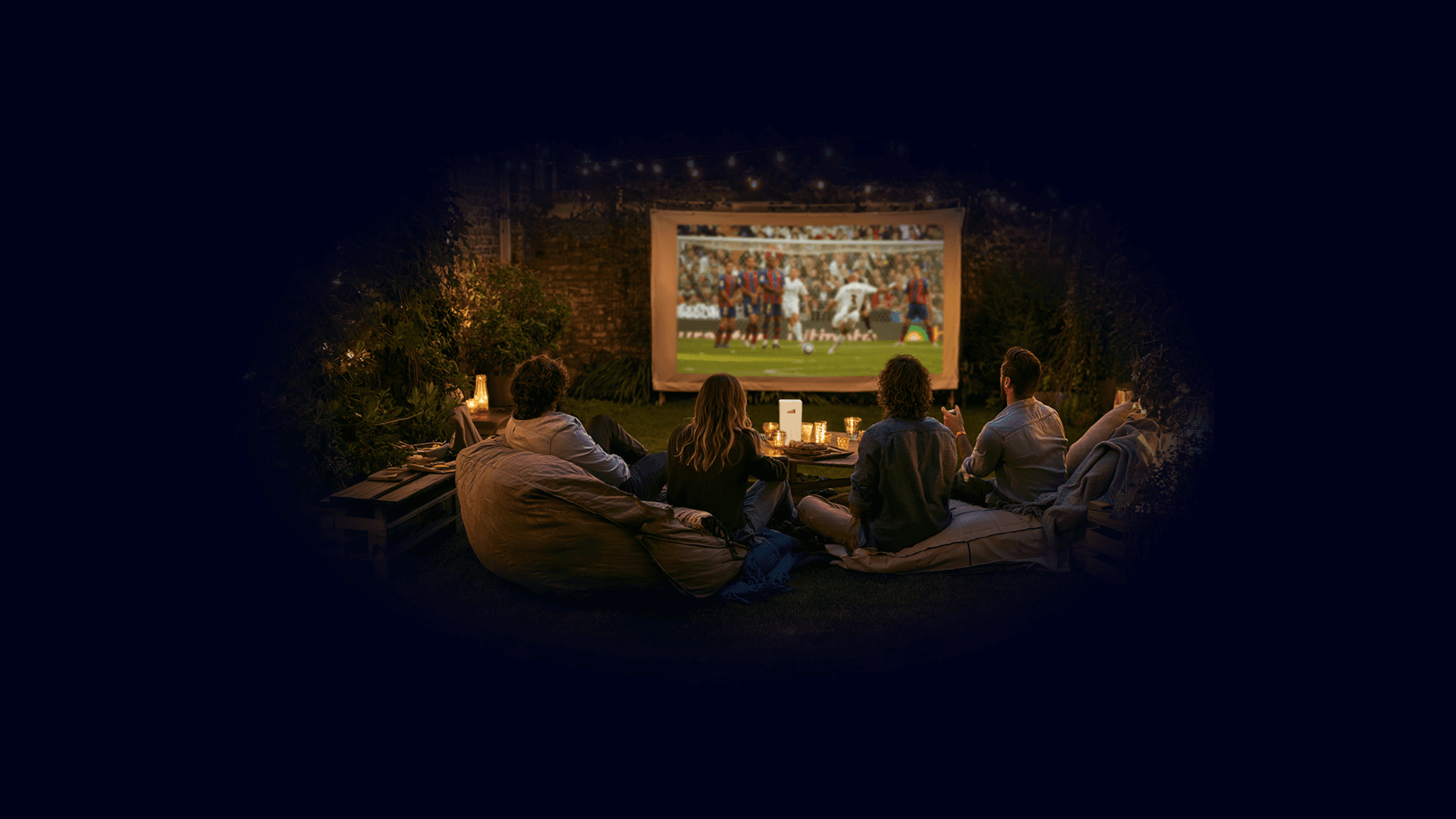 Friends watching football on an outdoor screen at night, TADAAM modem on the table.