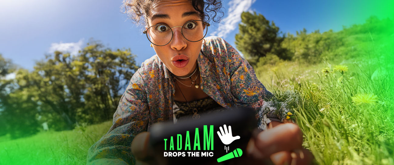 Une jeune femme surprise avec des lunettes qui regarde l'objectif depuis l'herbe, à côté du logo TADAAM 'Drops the Mic' en vert et blanc.