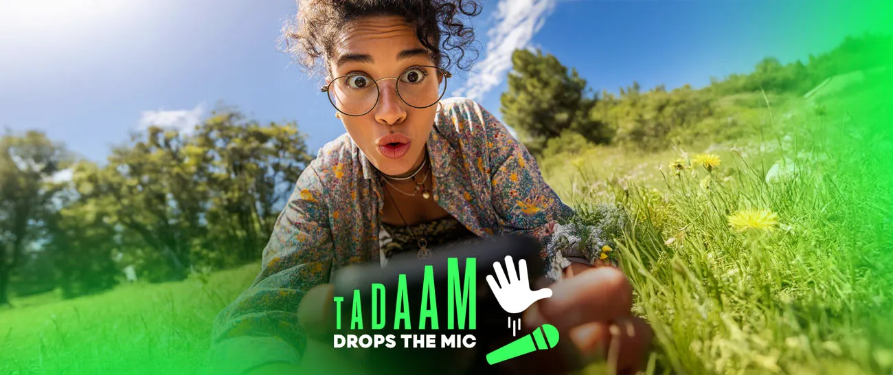 Surprised young woman in a grassy field with the TADAAM “Drops the Mic” campaign logo.