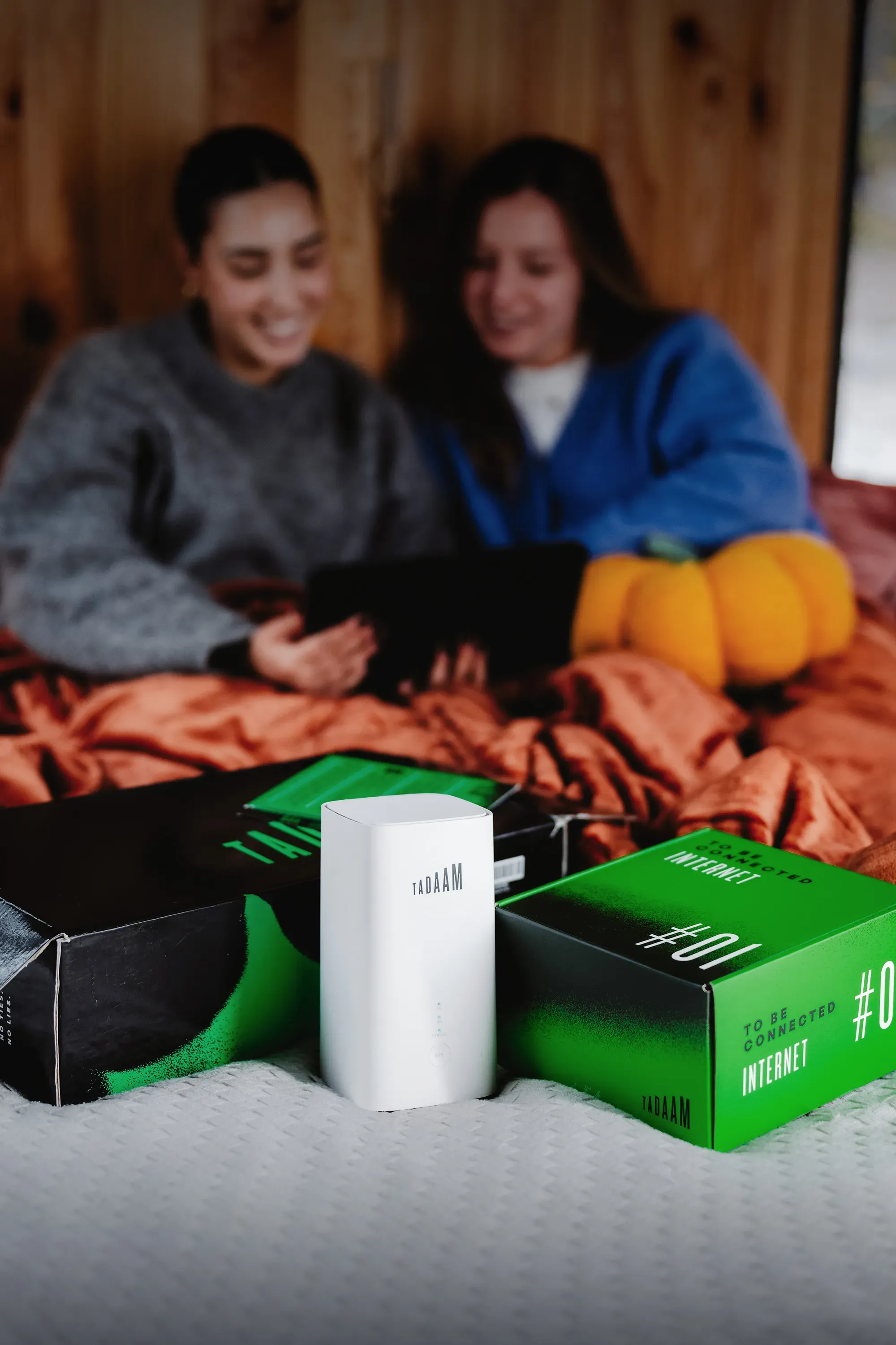 An image of two girls watching TV, with TADAAM modem and package in front of them.