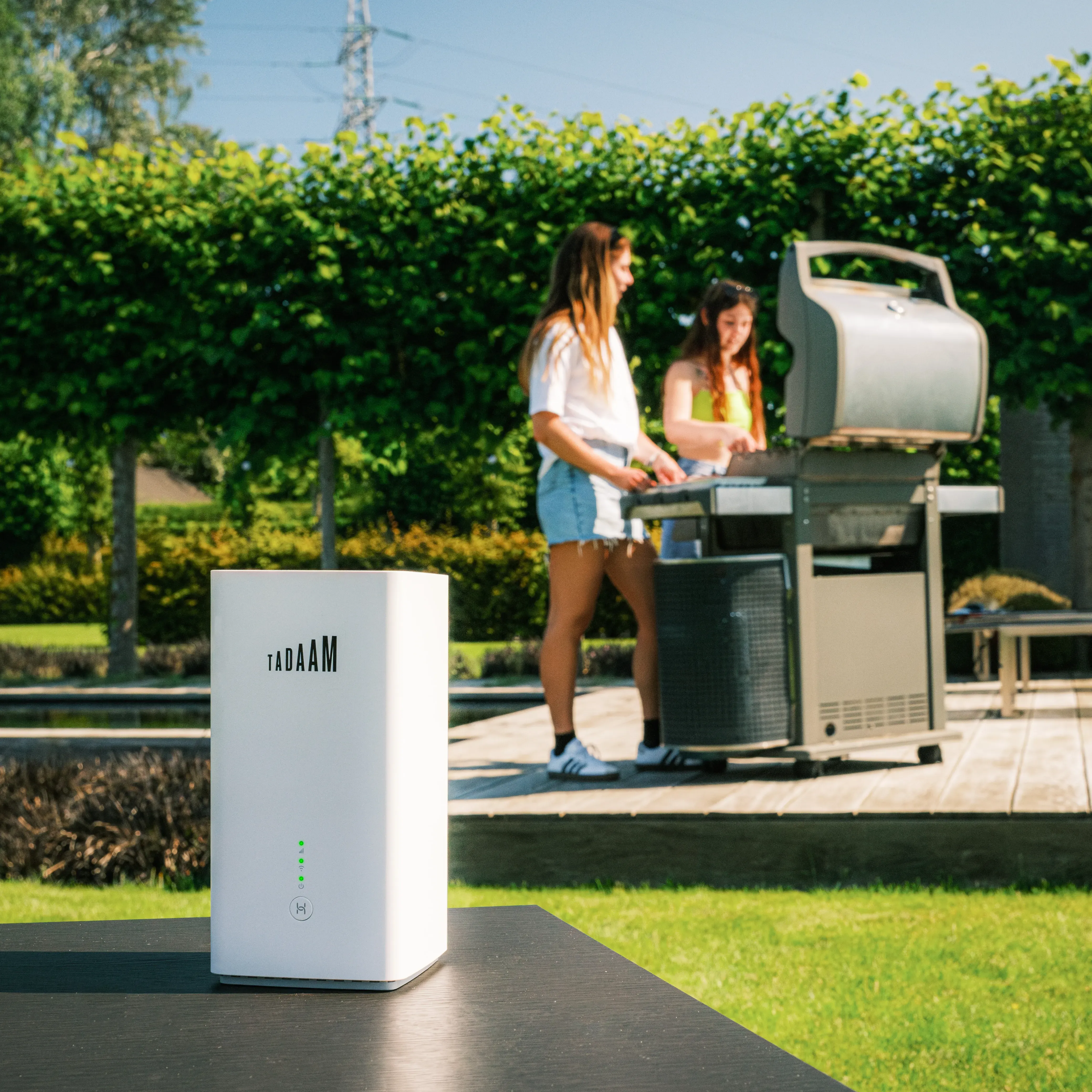 An image with two girls doing a BBQ on a sunny day, with a TADAAM's modem on the first plan.